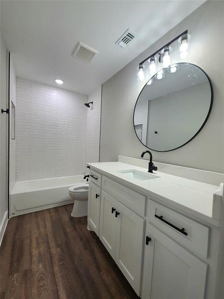 Guest Full bathroom with hardwood / wood-style floors, tiled shower / bath combo, vanity, and toilet