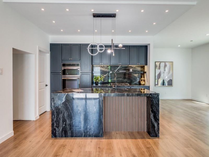 Kitchen with stainless steel double oven, hanging light fixtures, a large island with sink, and light hardwood / wood-style floors