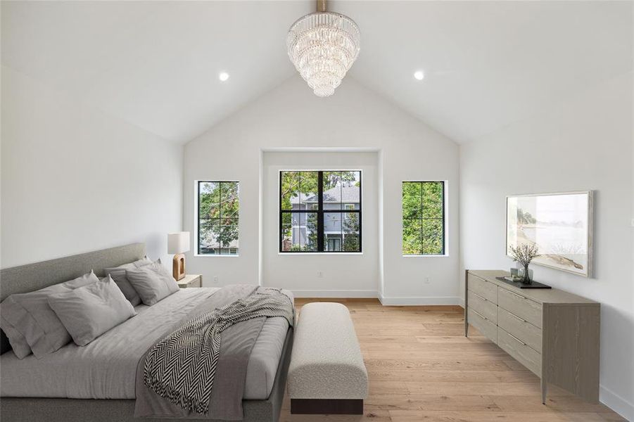 *Virtually rendered* The second-floor primary retreat features engineered white oak flooring, designer neutral wall paint, and recessed LED lighting. The space is enhanced by a vaulted ceiling with stained beam detail and a designer crystal chandelier. A trio of windows provides northern exposure, filling the room with natural light.