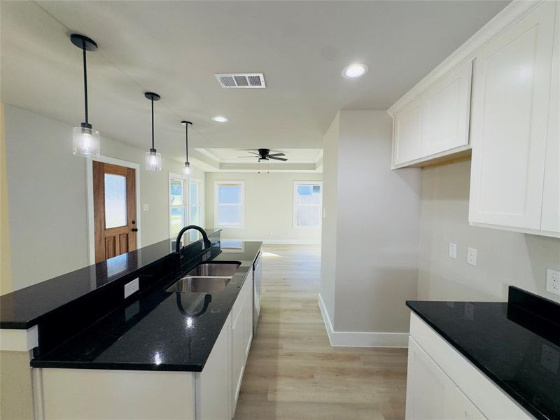 Kitchen with white cabinets, an island with sink, hanging light fixtures, sink, and light hardwood / wood-style flooring