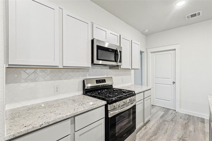 Kitchen with light hardwood / wood-style flooring, white cabinets, backsplash, light stone countertops, and appliances with stainless steel finishes