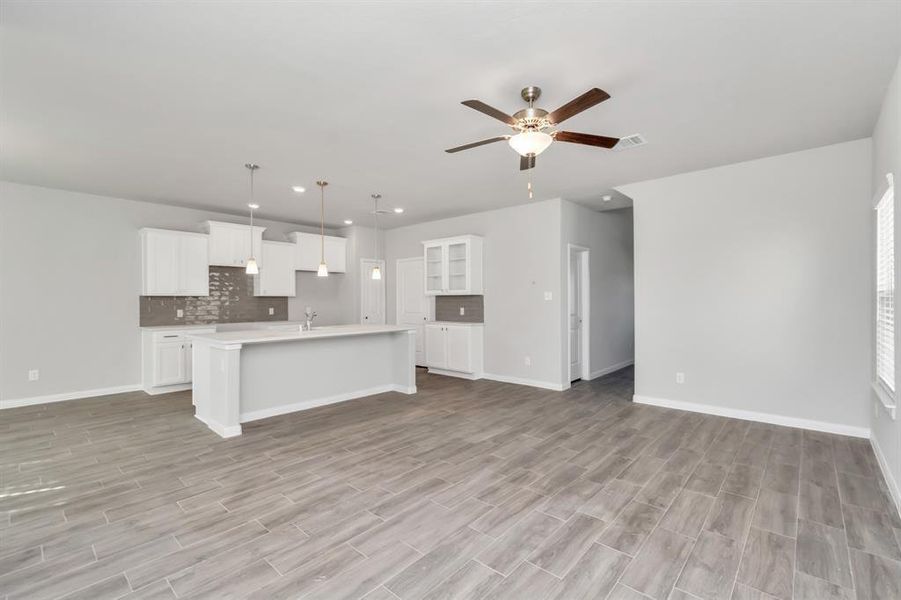 Enjoy the freedom and flexibility of open-concept living in this spacious kitchen and living area. The modern kitchen, complete with sleek white cabinetry, a large island, and pendant lighting, flows seamlessly into the expansive living space. This layout is perfect for entertaining or spending quality time with family, offering ample room for both dining and relaxation in a bright, airy environment. **This image is from another Saratoga Home with similar floor plan and finishes, not the June floorplan.**