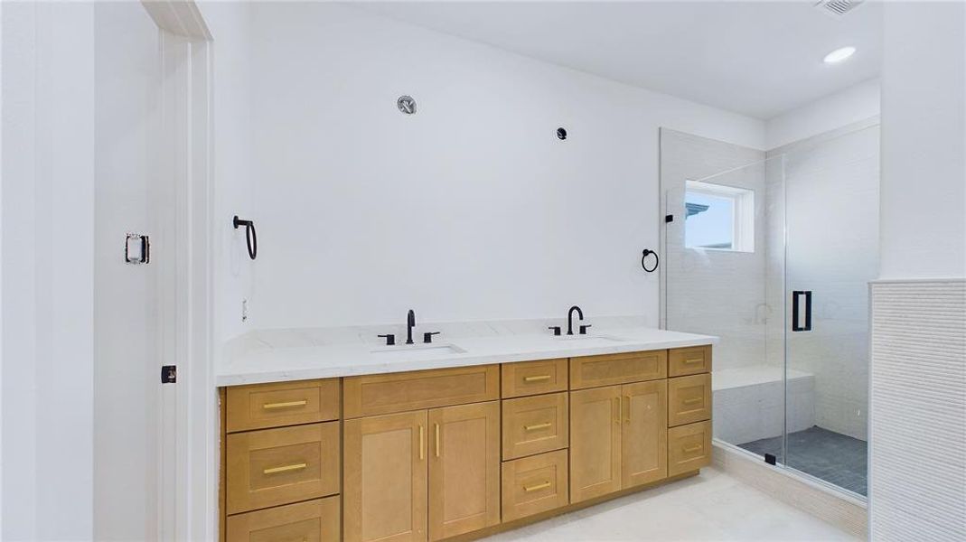 Primary bathroom offers a spacious dual vanity with under-mount sinks, and black faucets. Thoughtfully laid out cabinetry combines drawers with cabinets to leave no space wasted.