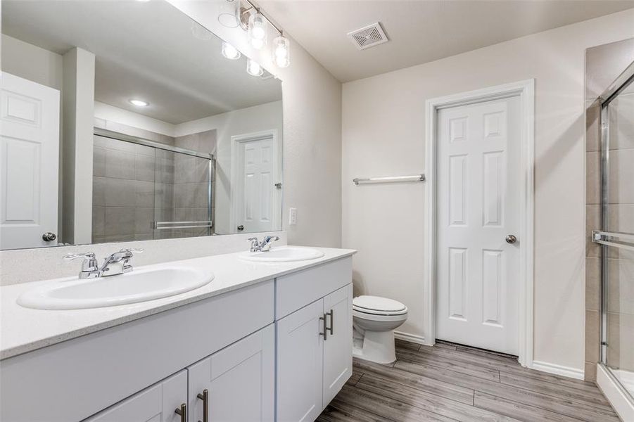 Bathroom with vanity with extensive cabinet space, double sink, an enclosed shower, and toilet