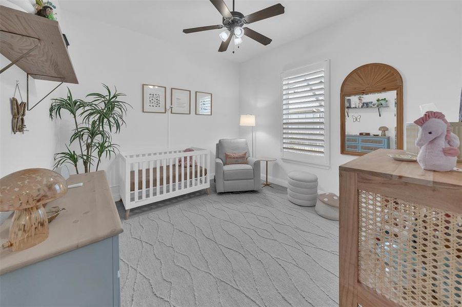 Carpeted bedroom with a nursery area and ceiling fan