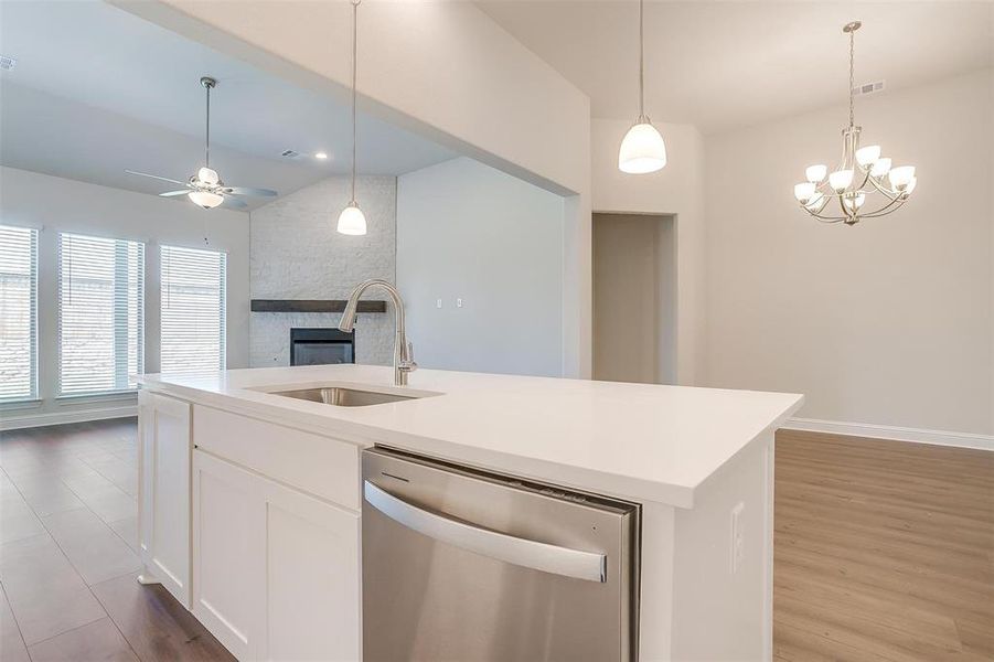 Kitchen featuring hardwood / wood-style flooring, ceiling fan with notable chandelier, dishwasher, sink, and a fireplace