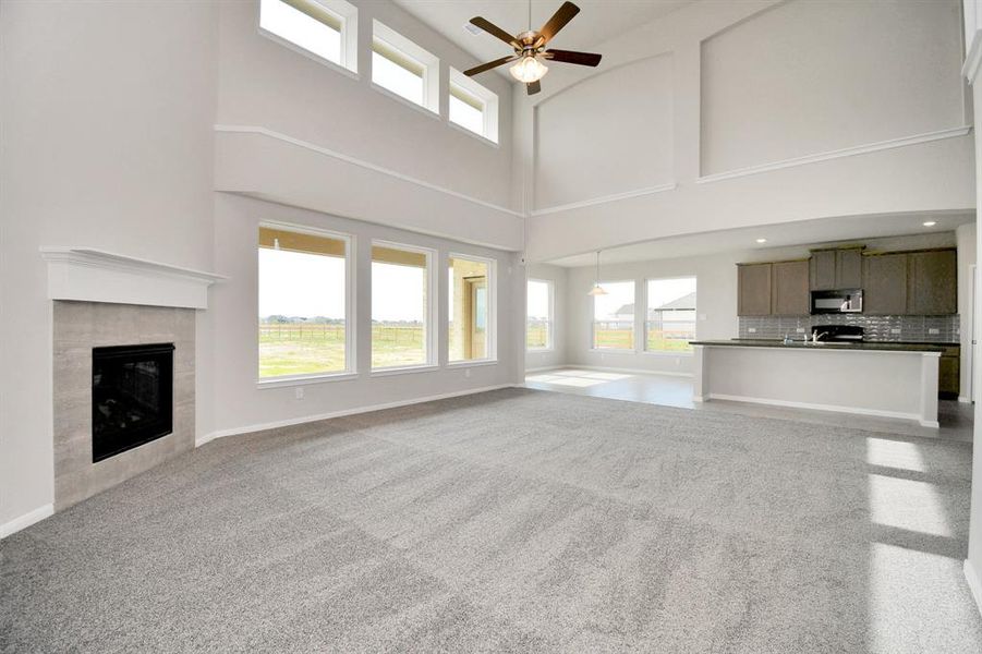 The living room features plush carpet, fireplace, high ceilings, large windows, and a ceiling fan.