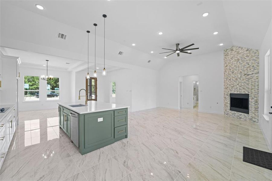 Kitchen featuring an island with sink, a fireplace, light tile floors, and ceiling fan with notable chandelier