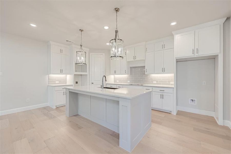 Kitchen with light hardwood / wood-style flooring, white cabinets, backsplash, and a kitchen island with sink