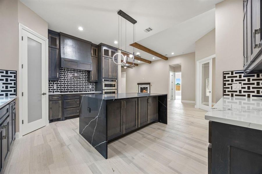 Kitchen featuring beamed ceiling, tasteful backsplash, premium range hood, decorative light fixtures, and light wood-type flooring