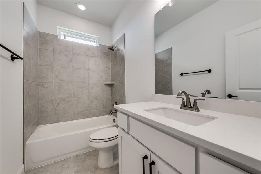 Full bathroom with vanity with extensive cabinet space, tile flooring, toilet, and tiled shower / bath combo