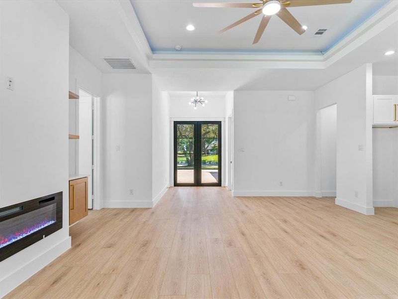 Unfurnished living room featuring french doors, ceiling fan with notable chandelier, light wood-type flooring, and a raised ceiling