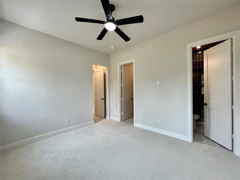 Unfurnished bedroom featuring ceiling fan, ensuite bath, light carpet, and a walk in closet