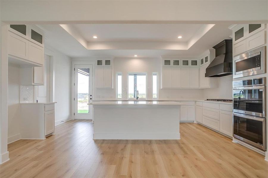 Kitchen featuring a kitchen island, custom exhaust hood, stainless steel appliances, and white cabinets