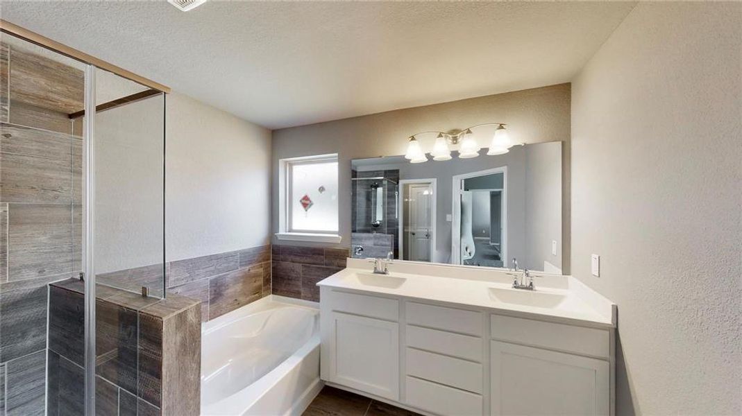 This modern primary bathroom is designed with relaxation in mind, offering a spacious walk-in shower, a deep soaking tub, and a double vanity with ample counter space. The elegant tile work and sleek fixtures add a touch of sophistication. This is a picture of an Elise Floor Plan with another Saratoga Homes.