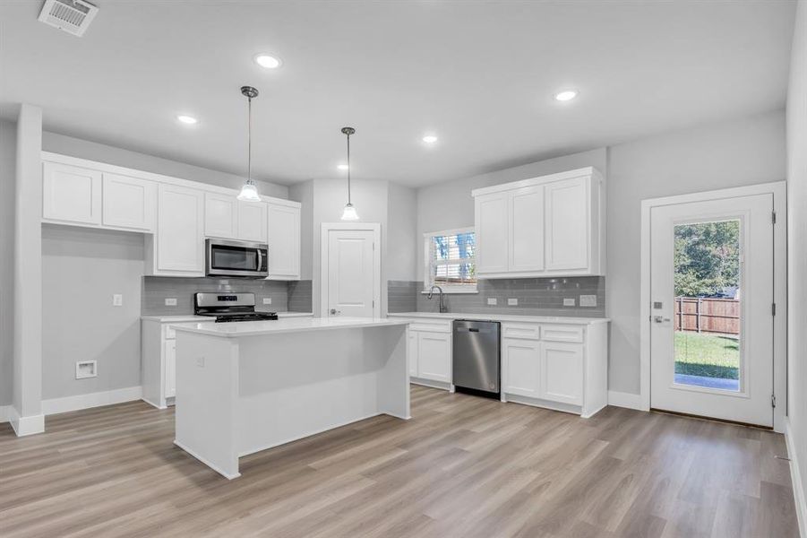 Kitchen with a wealth of natural light, appliances with stainless steel finishes, light wood-type flooring, and a kitchen island