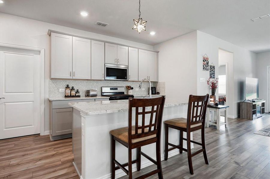 Kitchen featuring a breakfast bar area, tasteful backsplash, light stone counters, stainless steel appliances, and hardwood / wood-style floors