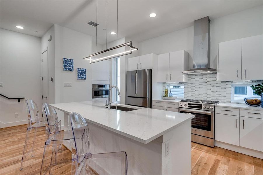 Kitchen featuring pendant lighting, a kitchen island with sink, sink, wall chimney exhaust hood, and appliances with stainless steel finishes