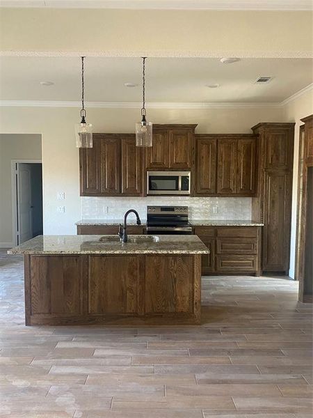 Kitchen featuring light stone counters, a kitchen island with sink, appliances with stainless steel finishes, and dark brown cabinetry