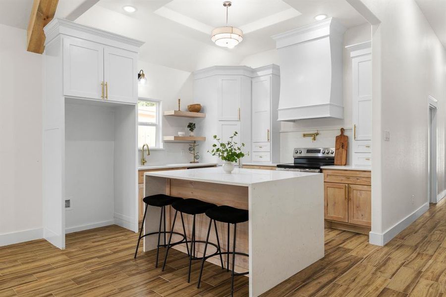Kitchen featuring white cabinets, premium range hood, light hardwood / wood-style floors, a kitchen island, and a raised ceiling