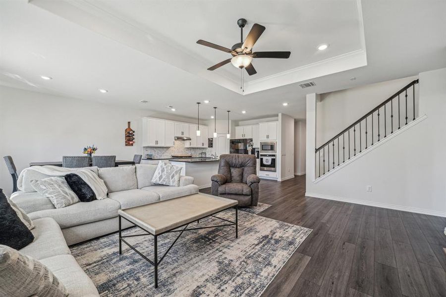 Living room with ornamental molding, dark hardwood / wood-style flooring, ceiling fan, and a raised ceiling