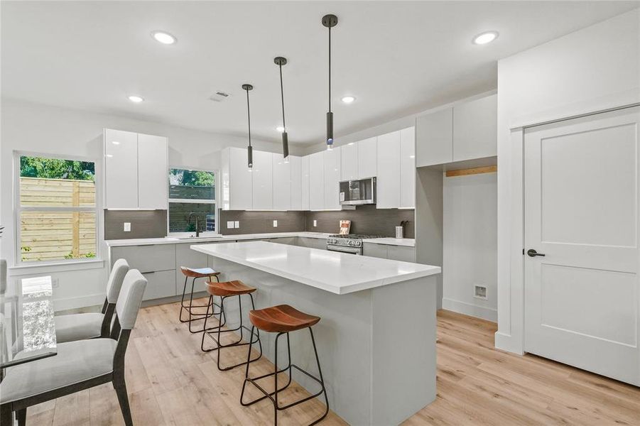 Kitchen with white cabinets, appliances with stainless steel finishes, decorative light fixtures, and a center island