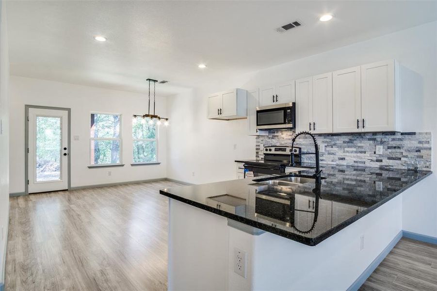 Kitchen with light wood-type flooring, white cabinetry, kitchen peninsula, hanging light fixtures, and stainless steel appliances