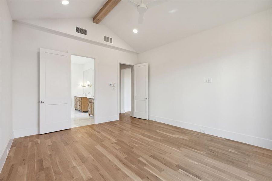 Unfurnished bedroom featuring light hardwood / wood-style floors, lofted ceiling with beams, ensuite bath, and ceiling fan