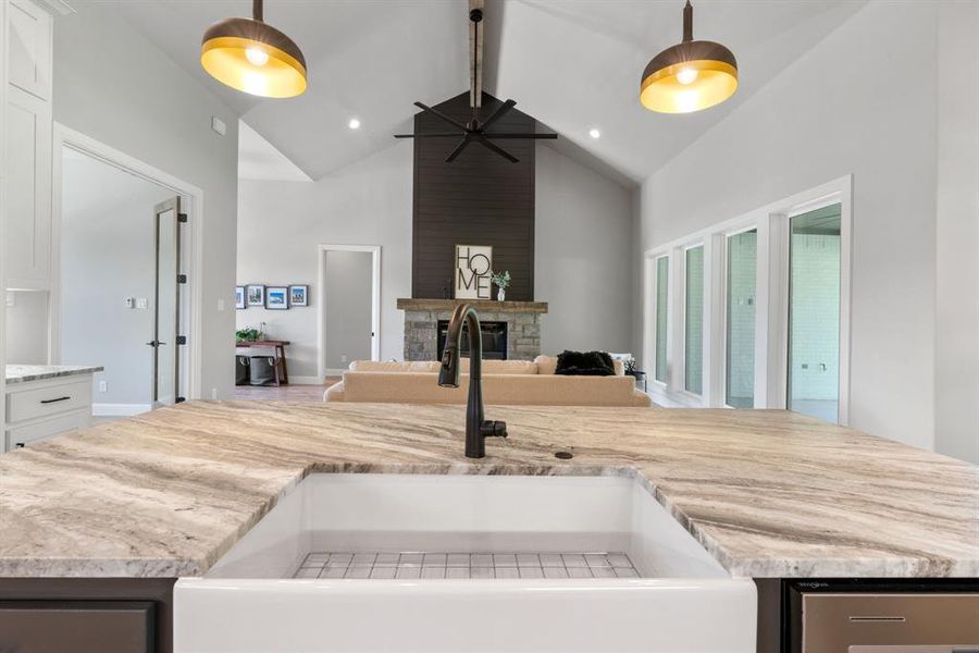 Kitchen with a kitchen island, a stone fireplace, beam ceiling, white cabinets, and sink