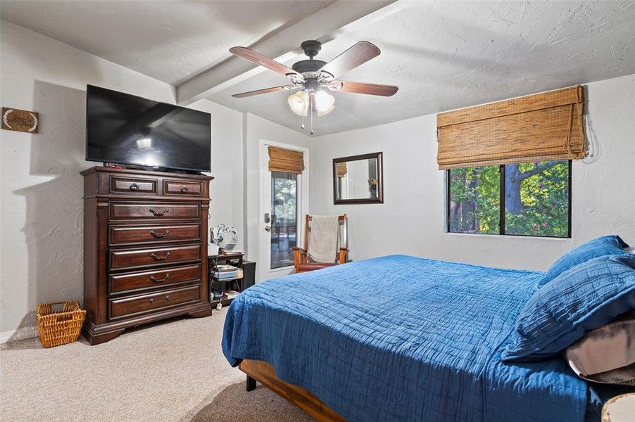 Bedroom featuring multiple windows, ceiling fan, carpet flooring, and beam ceiling