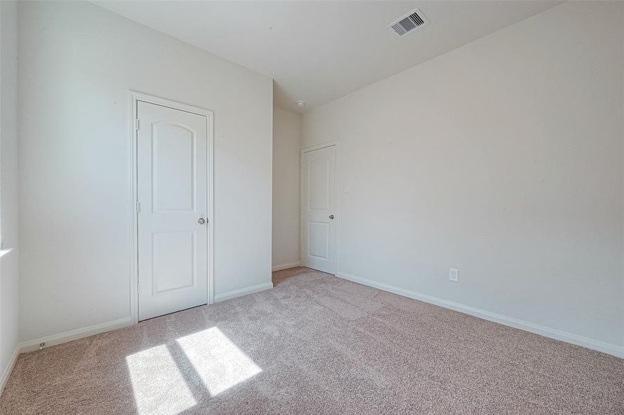 Empty room with beige carpet, white walls, sunlight through window, and two closed doors.