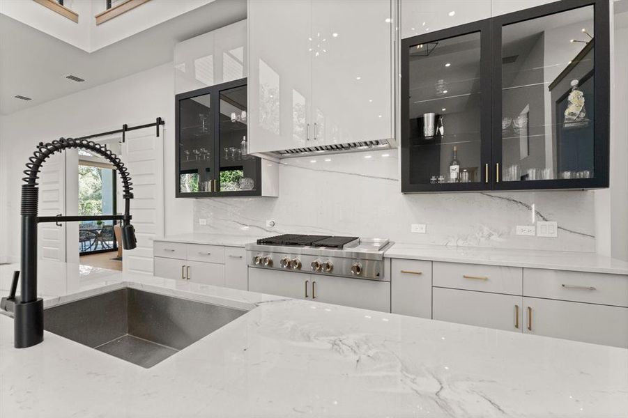 Slab style backsplash and two-tone glass front cabinets give this kitchen a sleek look!