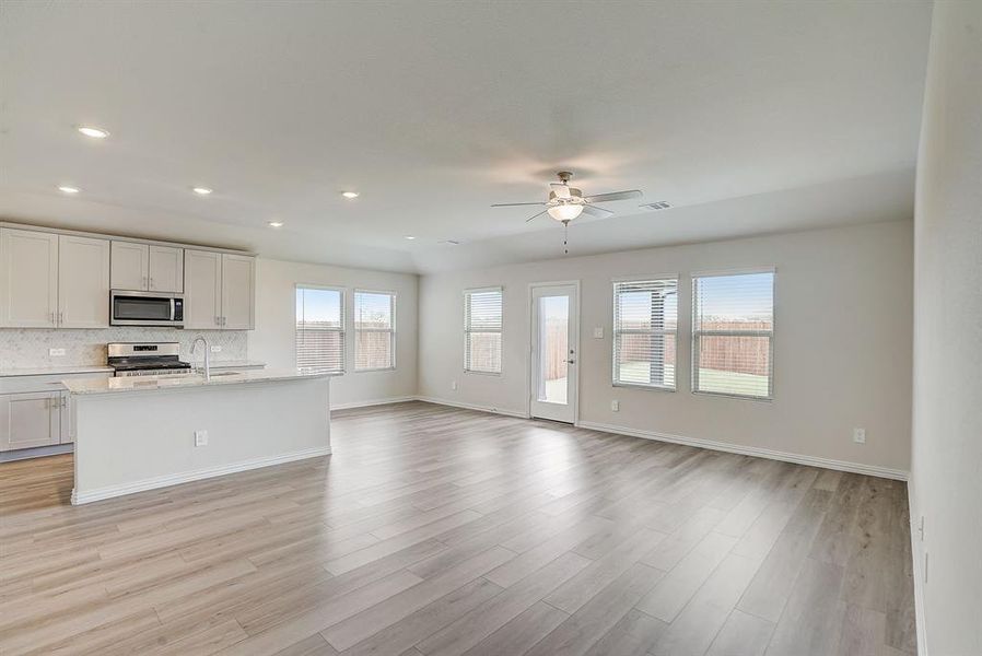 Kitchen with ceiling fan, light hardwood / wood-style flooring, stainless steel appliances, backsplash, and white cabinets