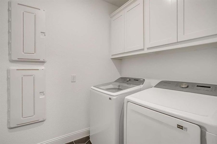 Clothes washing area with tile patterned floors, washing machine and dryer, electric panel, and cabinets