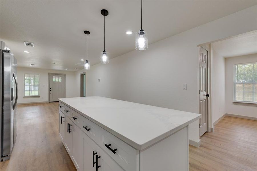 Kitchen featuring stainless steel refrigerator with ice dispenser, light hardwood / wood-style floors, hanging light fixtures, white cabinetry, and a center island