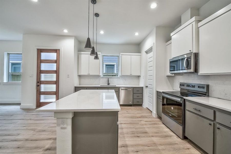 Kitchen with appliances with stainless steel finishes, a kitchen island, tasteful backsplash, and light hardwood / wood-style flooring