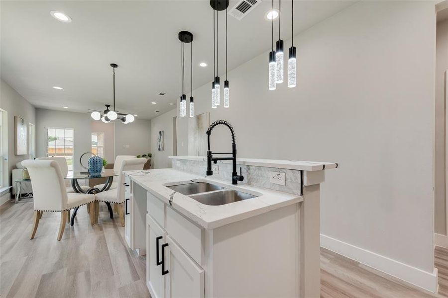 Kitchen featuring decorative light fixtures, an island with sink, light wood-type flooring, sink, and light stone countertops