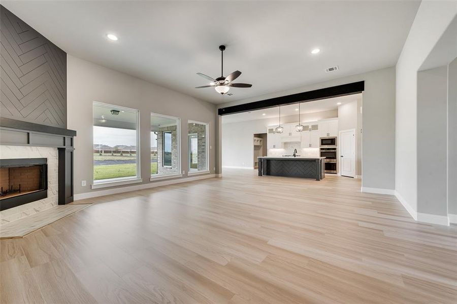 Unfurnished living room with ceiling fan, sink, a tiled fireplace, and light hardwood / wood-style floors