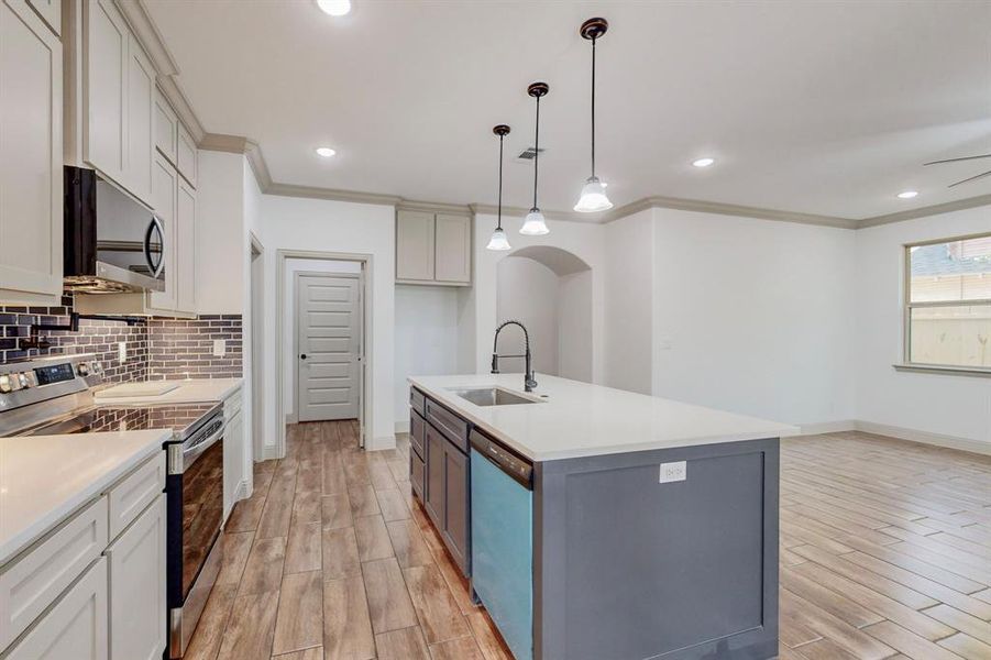 Kitchen featuring appliances with stainless steel finishes, light hardwood / wood-style flooring, sink, decorative backsplash, and a kitchen island with sink