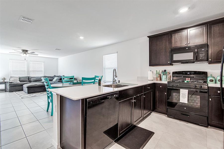 Kitchen with black appliances, sink, dark brown cabinets, kitchen peninsula, and ceiling fan