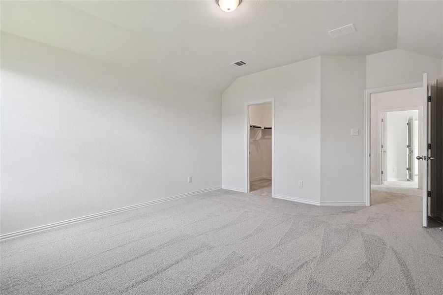 Unfurnished bedroom with a closet, light colored carpet, lofted ceiling, and a spacious closet