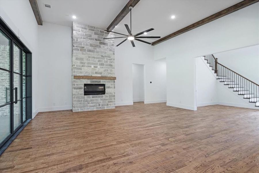 Unfurnished living room featuring beamed ceiling, a large fireplace, ceiling fan, and hardwood / wood-style flooring