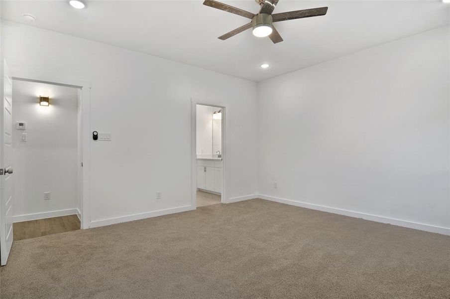 Unfurnished bedroom featuring light colored carpet, ensuite bath, and ceiling fan