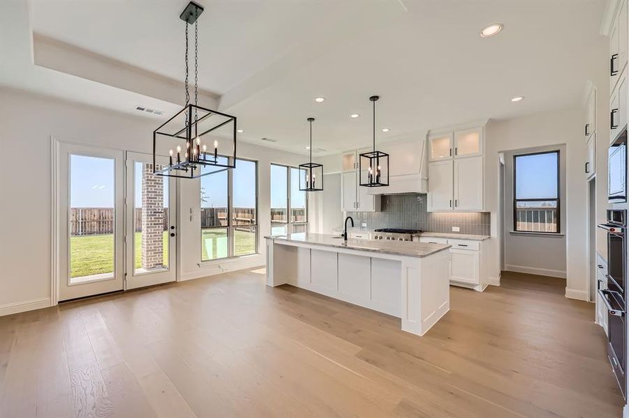 Kitchen featuring white cabinetry, decorative light fixtures, light hardwood / wood-style flooring, decorative backsplash, and a kitchen island with sink