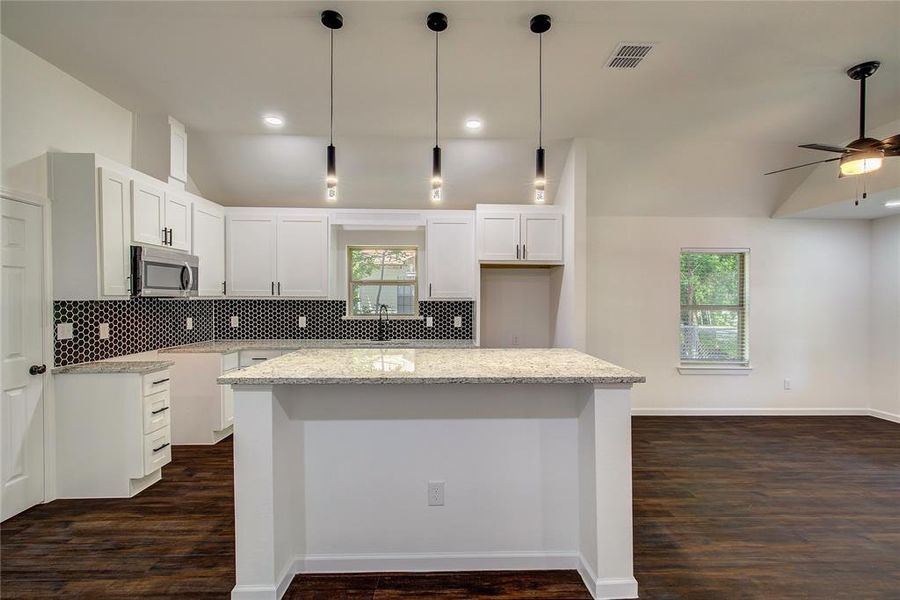 Kitchen with a wealth of natural light, tasteful backsplash, dark wood-type flooring, and pendant lighting