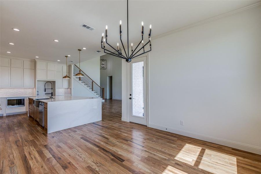 Kitchen with pendant lighting, a chandelier, light hardwood / wood-style flooring, built in microwave, and a spacious island