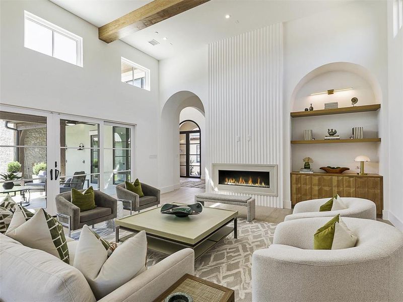 Living room with built in shelves, beamed ceiling, a fireplace, a towering ceiling, and light hardwood / wood-style floors