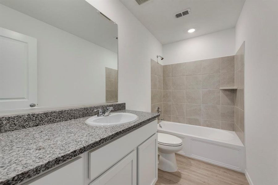 Full bathroom featuring vanity, tiled shower / bath, hardwood / wood-style floors, and toilet