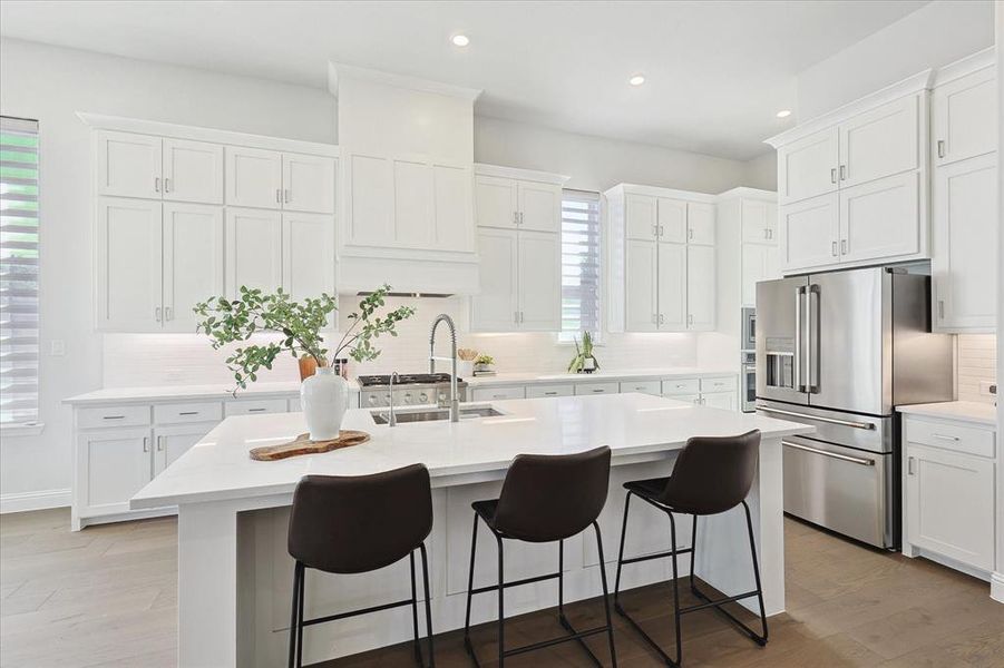 Kitchen with white cabinetry, a center island with sink, high end refrigerator, and backsplash