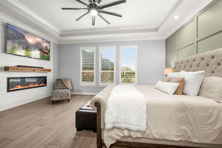 Magnificent primary bedroom features accent walls, no-heat option fireplace with cedar beam and shiplap, tray ceiling, crown molding and accent lights